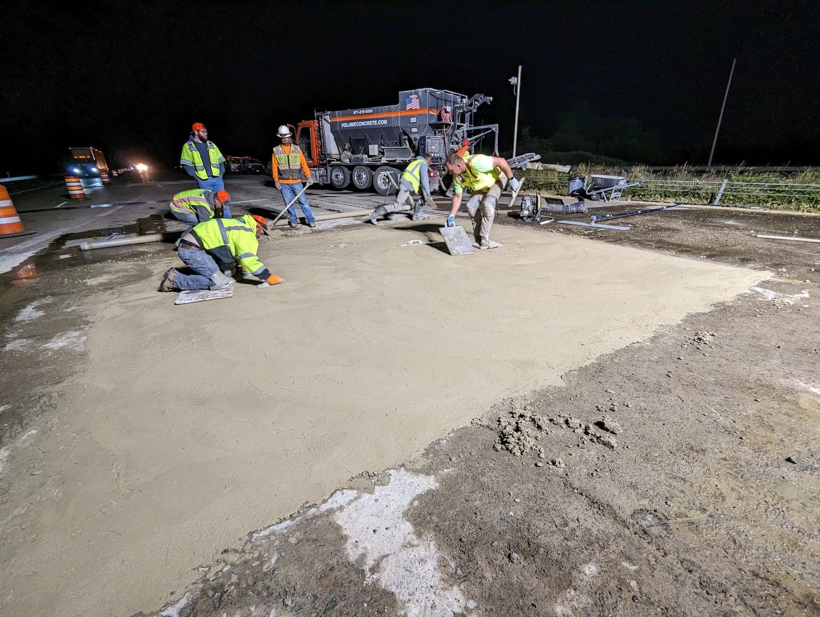Crew finishing a night road pour with a branded Volume Concrete volumetric mixer