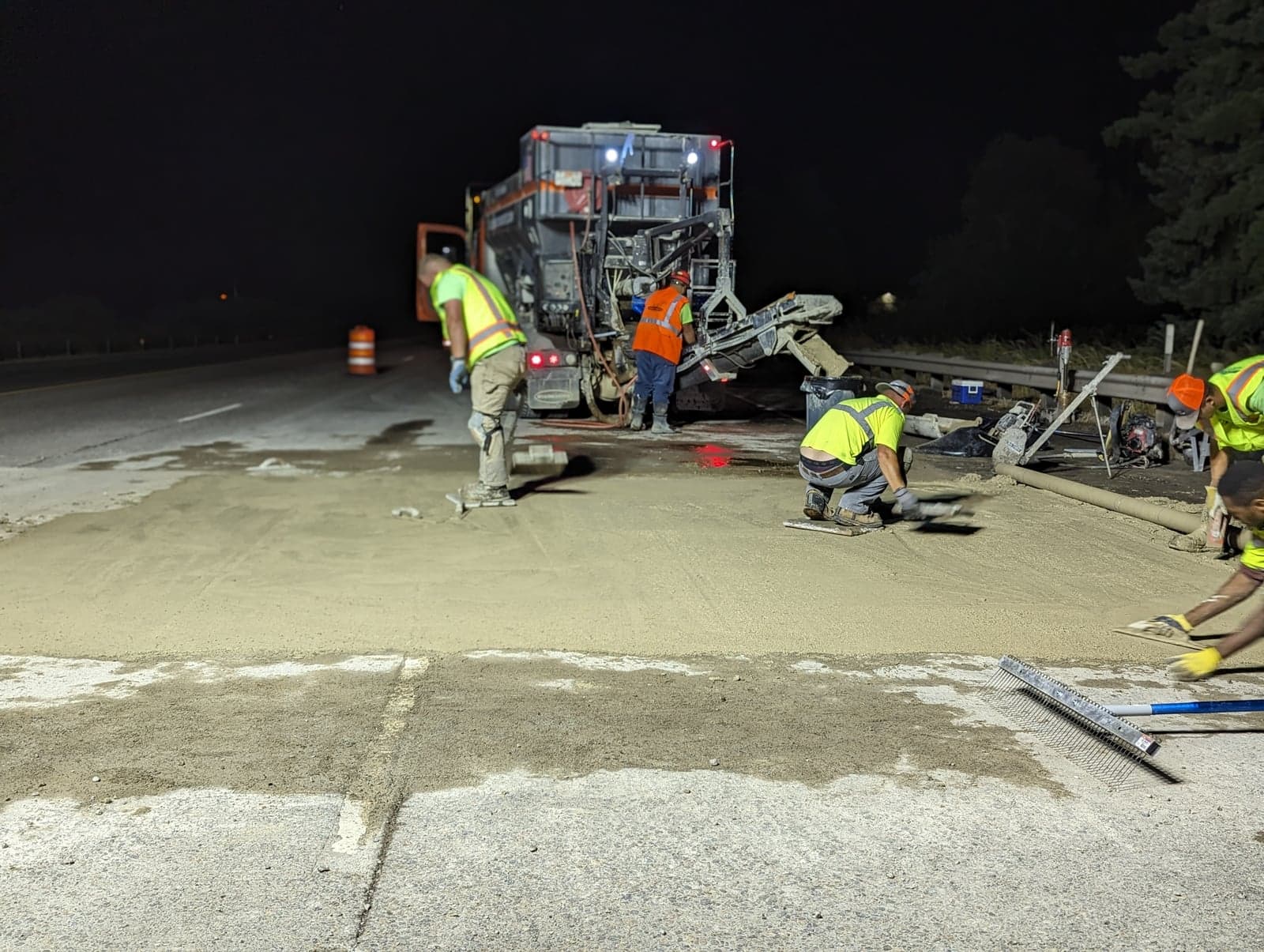 Rear of a volumetric mixer pouring at night while the crew levels the patch