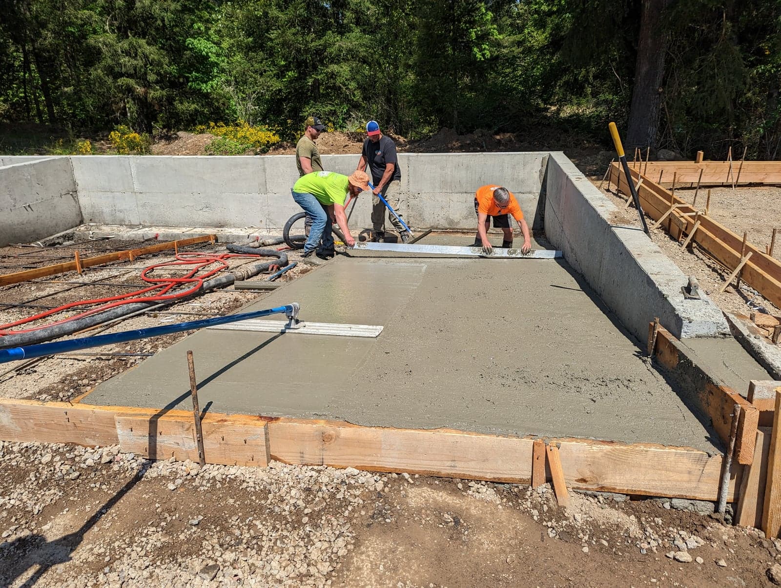 Crew bull-floating and screeding a sunny foundation slab pour