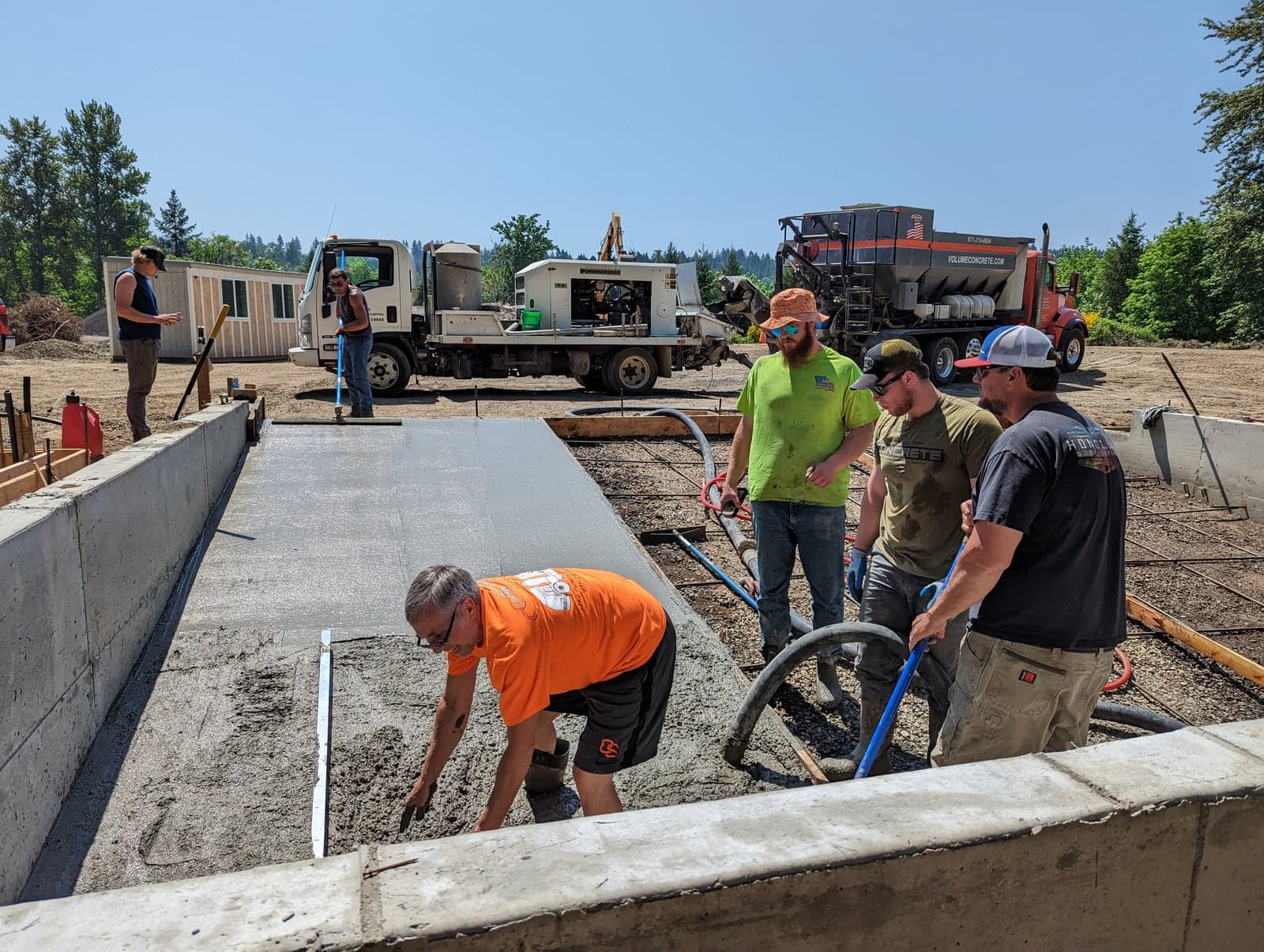 Orange Volume Concrete volumetric mixer and white pump truck on a sunny slab pour